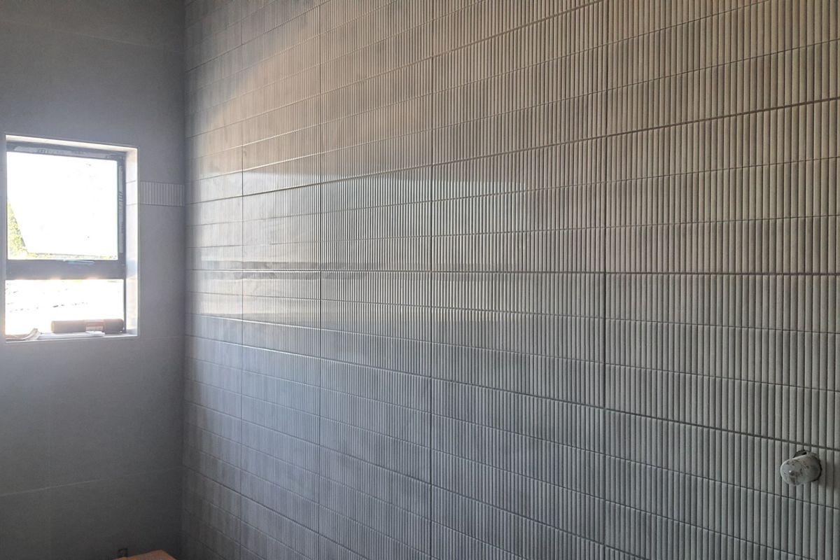 A modern bathroom space featuring contemporary textured wall tiling and a window, currently in a clean, unfinished state ready for final fixtures.