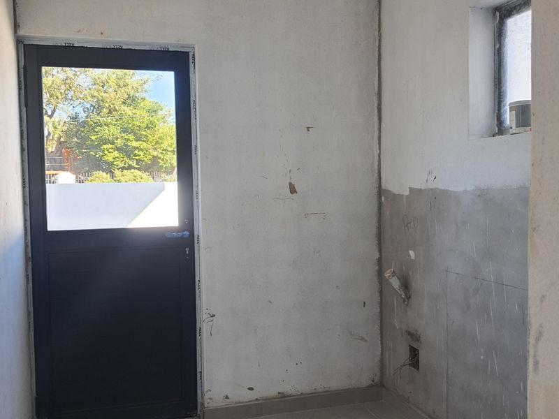 An unfinished utility or laundry space featuring tiled flooring, plumbing connections, and an exterior access door, requiring cosmetic completion and wall finishing.