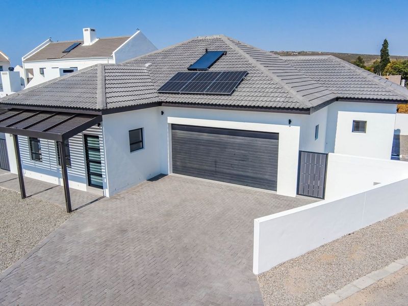Aerial view of a modern house featuring a paved driveway, double garage, pergola, and roof-mounted solar panels and geyser.