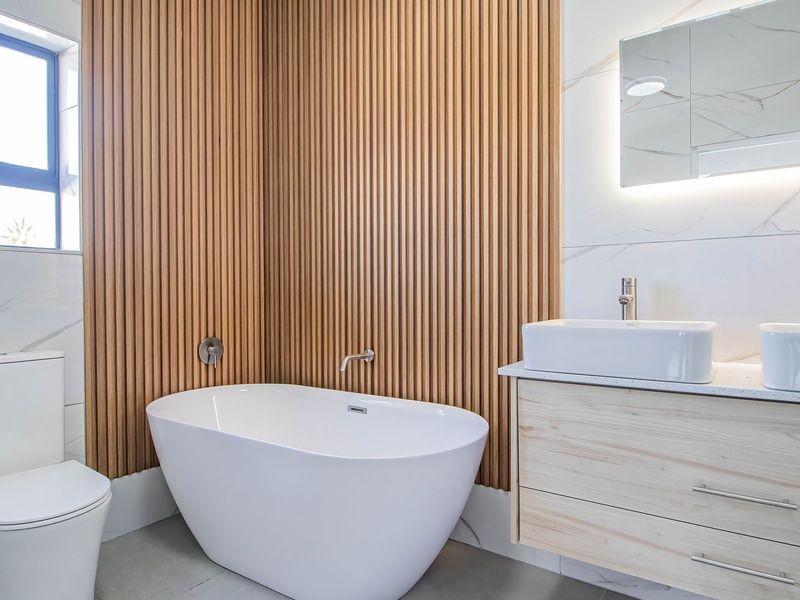 Modern bathroom featuring a freestanding bathtub, double vanity with vessel sinks, slatted timber feature wall, and marble-look tiling.