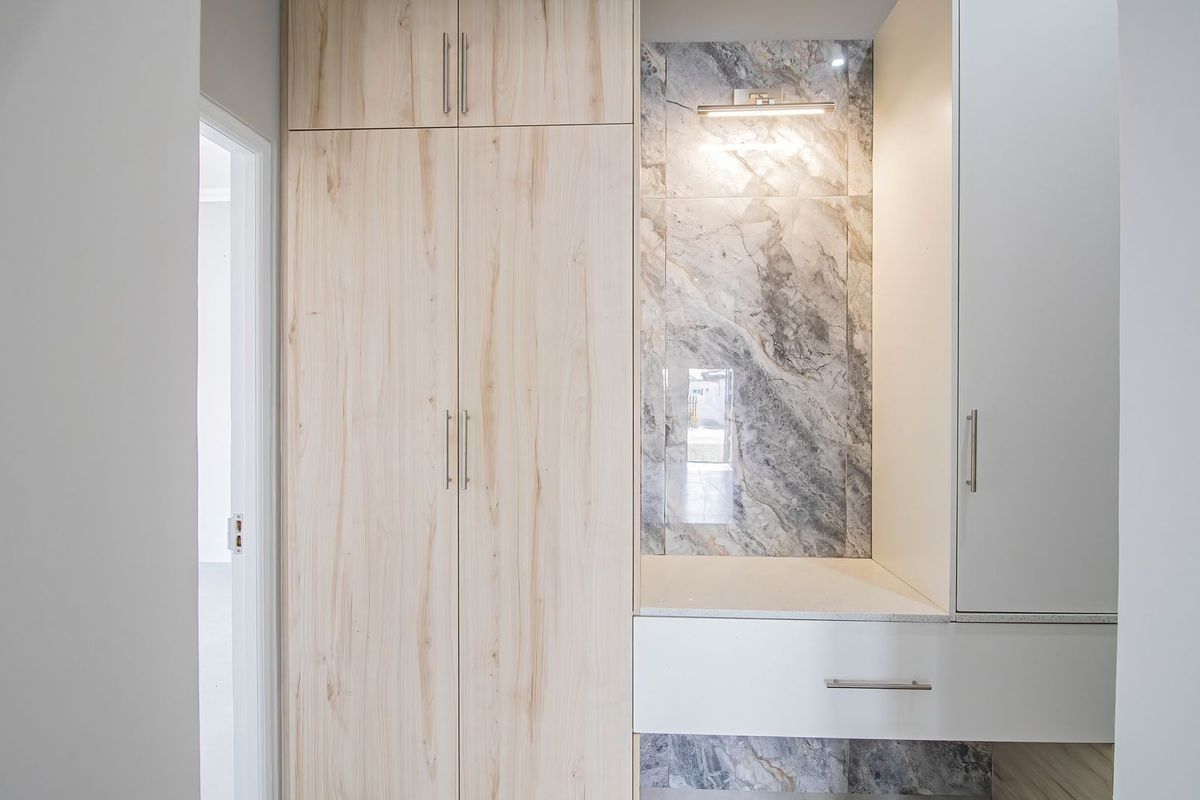 Modern bedroom featuring custom built-in cabinetry with light wood grain finish, stone vanity surface, and elegant marble-look wall tiling with integrated lighting.