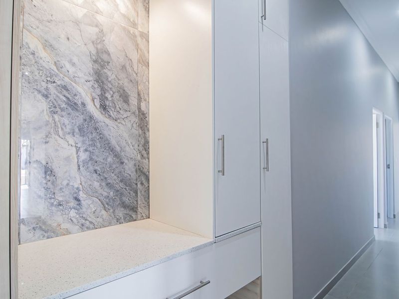 A modern, well-lit hallway featuring sleek built-in cabinetry with a stone countertop and elegant marble-look wall tiling.