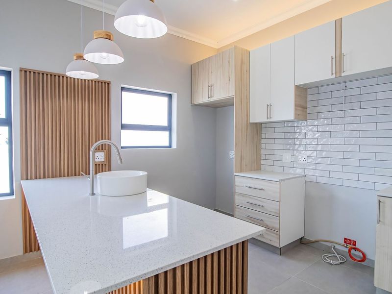 Modern kitchen featuring a quartz island with sink, subway tile backsplash, custom cabinetry, and stylish slatted wood accents.