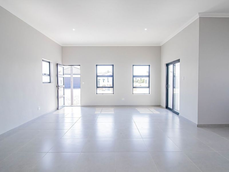 A bright, spacious, and empty living area featuring neutral tiled flooring, modern aluminium window frames, and a sliding glass door leading to the exterior.