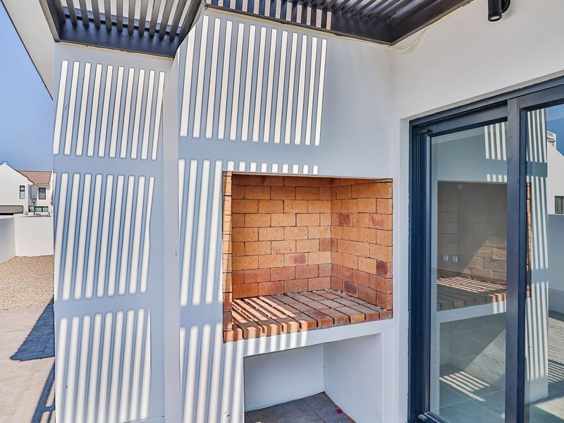 Covered patio area featuring a built-in brick braai, slatted pergola overhead, and large sliding glass doors leading into the home.