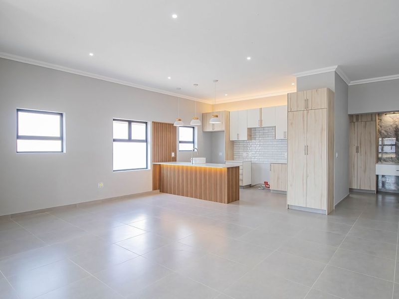 Spacious open-plan living area featuring a modern kitchen with light wood cabinetry, a central island, and neutral tiled flooring throughout.