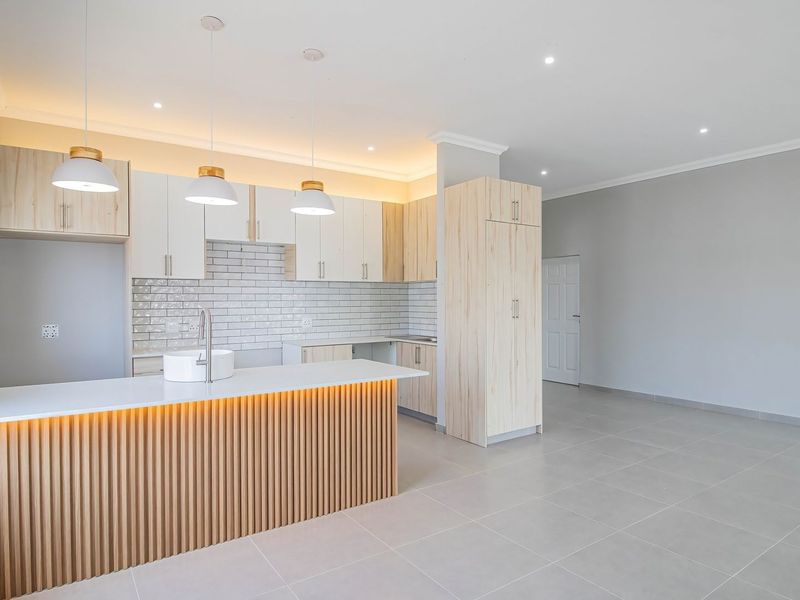 Modern open-plan kitchen featuring light wood cabinetry, a slatted kitchen island with integrated lighting, subway tile backsplash, and neutral tiled flooring.