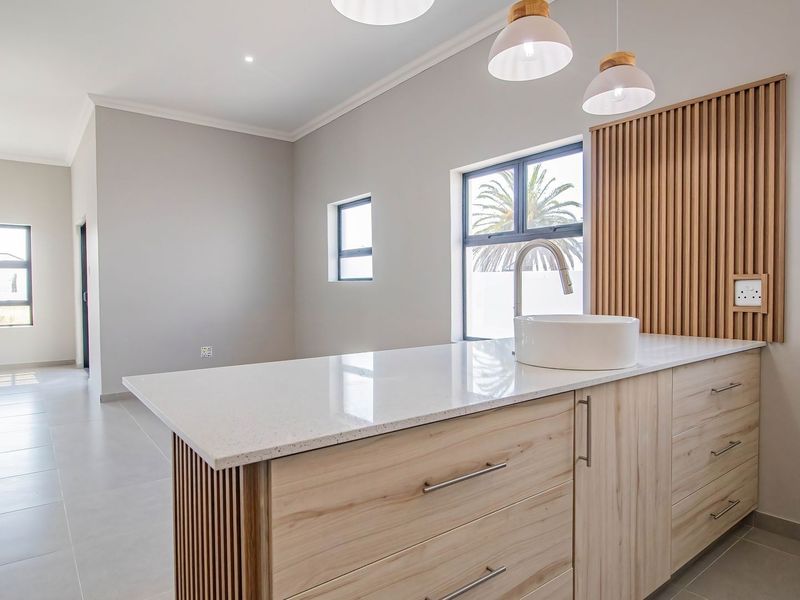Modern kitchen area featuring a central island with quartz countertop, vessel sink, light wood cabinetry, and decorative slatted wood wall paneling.