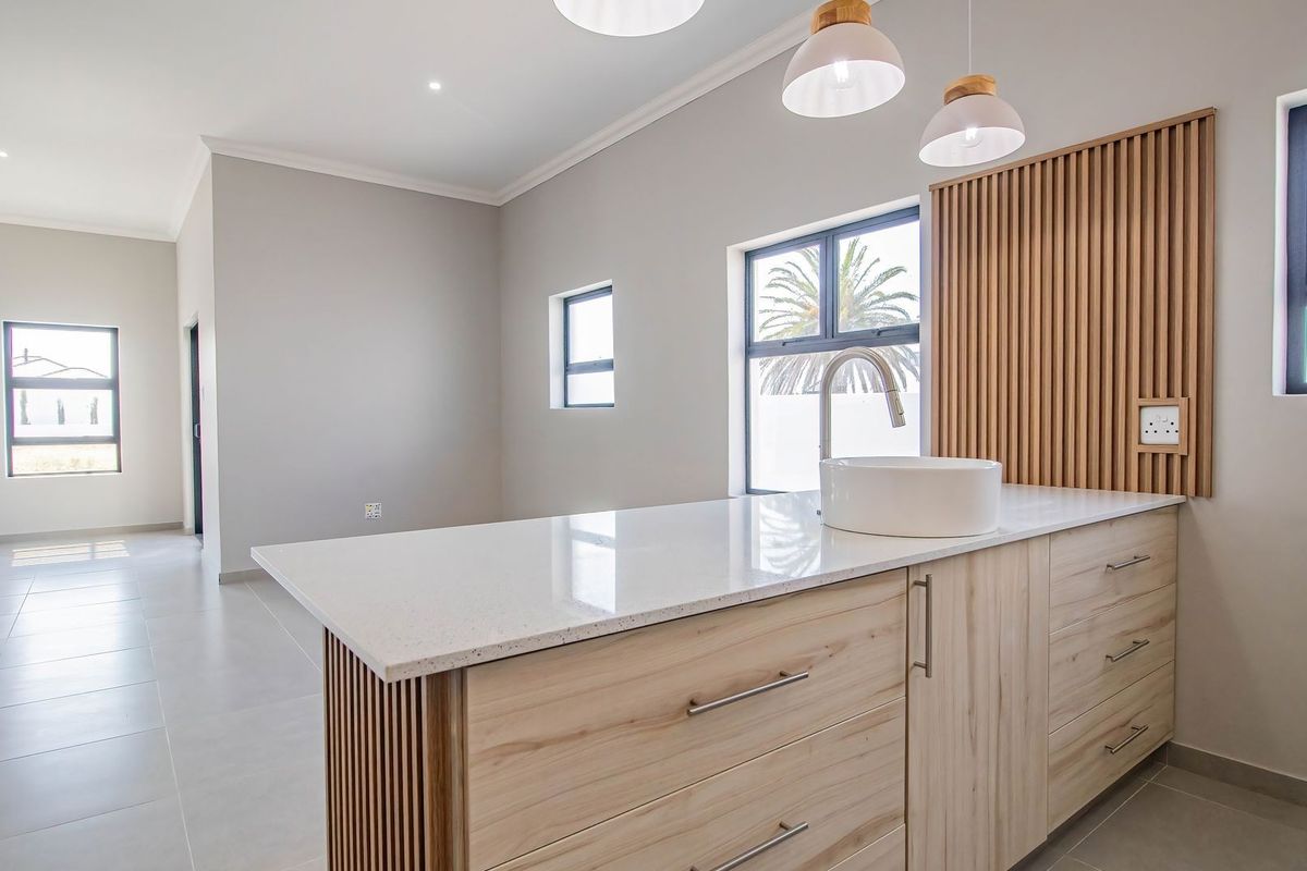 Modern kitchen area featuring a central island with quartz countertop, vessel sink, light wood cabinetry, and decorative slatted wood wall paneling.