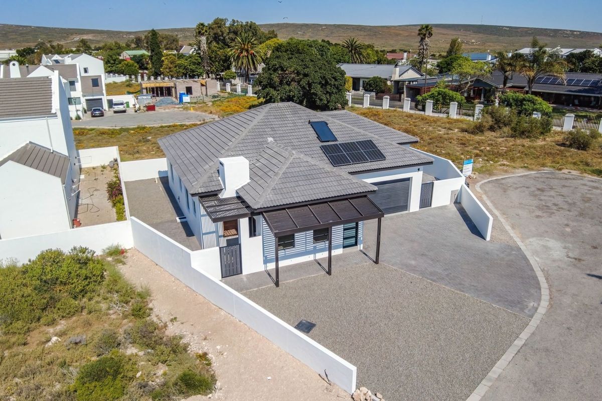 Aerial view of a modern single-story house featuring a tiled roof, solar panels, solar geyser, paved driveway, and secure boundary walls.