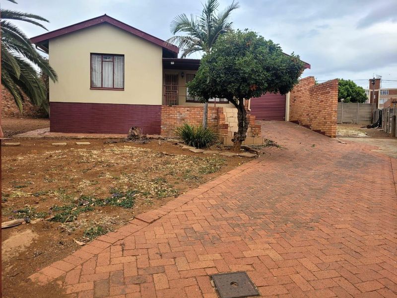 Front view of a detached house featuring a brick driveway, garage, and established garden area.