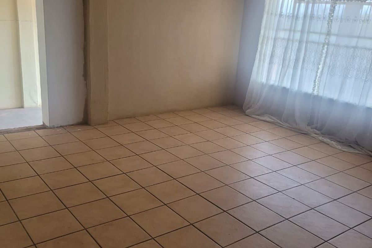 An empty living room featuring ceramic floor tiles, an exposed timber beam, and unfinished wall surfaces awaiting final paint or plastering.