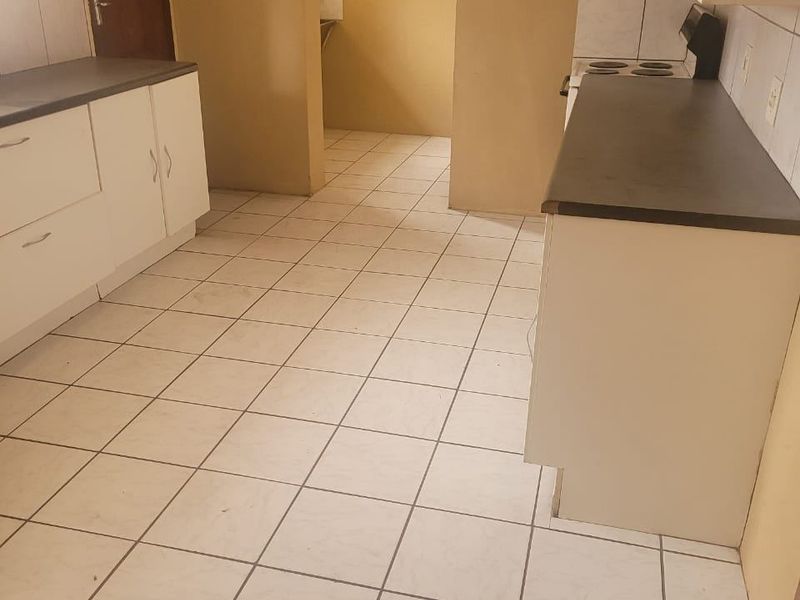 A functional kitchen featuring white cabinetry, dark laminate countertops, and tiled flooring, with an adjacent scullery area visible through the doorway.