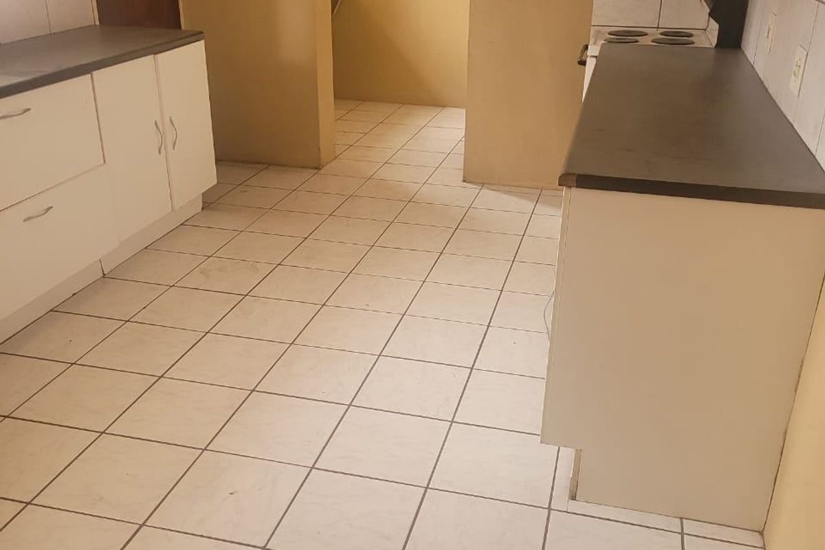 A functional kitchen featuring white cabinetry, dark laminate countertops, and tiled flooring, with an adjacent scullery area visible through the doorway.
