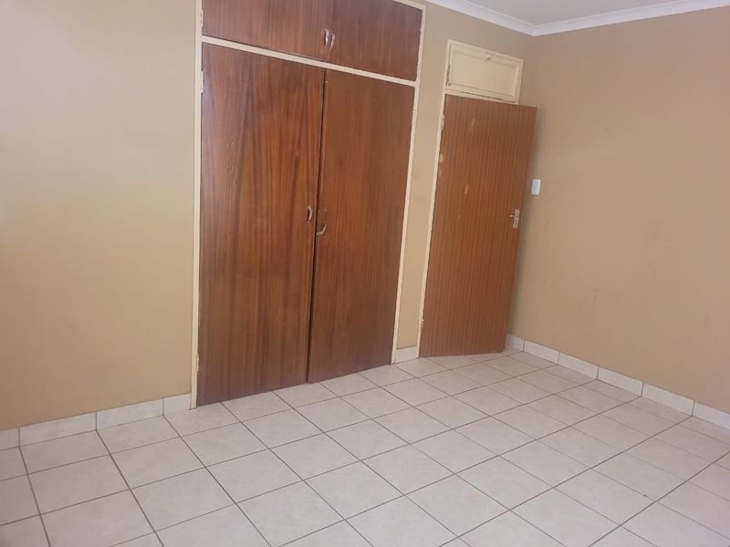 An empty bedroom featuring tiled flooring and built-in wooden cupboards, offering a blank canvas for renovation or interior design updates.