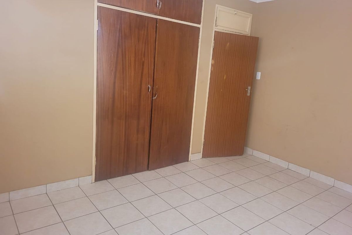 An empty bedroom featuring tiled flooring and built-in wooden cupboards, offering a blank canvas for renovation or interior design updates.