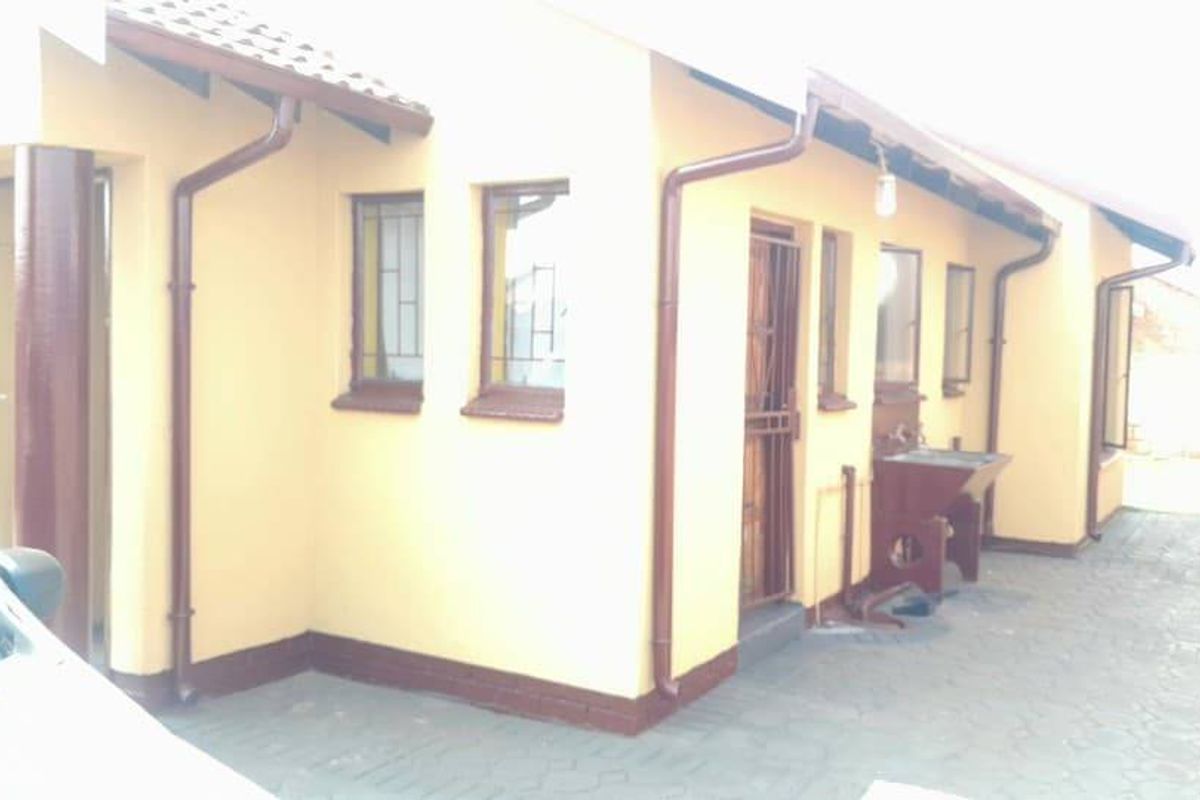 Side view of the house featuring a paved driveway, exterior utility sink, security gates, and downpipes.