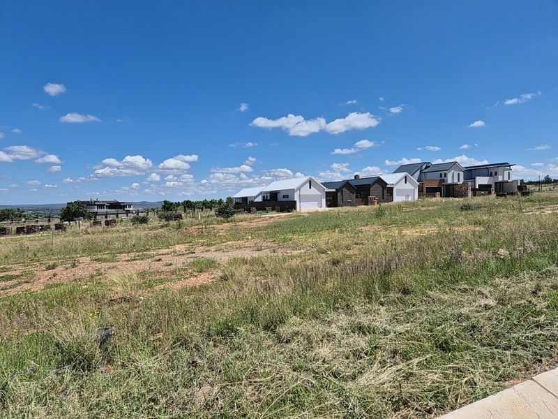 A view of a vacant residential plot situated within a developing estate, showcasing the surrounding neighborhood and open land.
