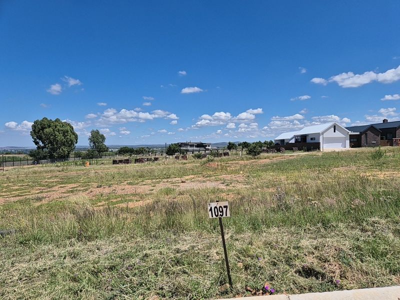 A vacant residential plot of land featuring natural grass coverage and a clear boundary marker, situated in a developing residential estate.