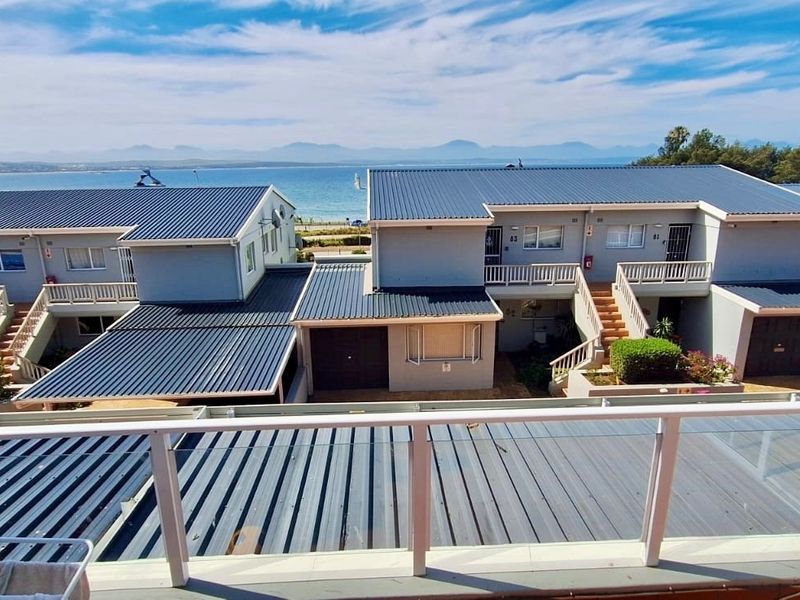Elevated view overlooking a residential apartment complex with metal roofing, featuring a clear coastal and mountain backdrop.