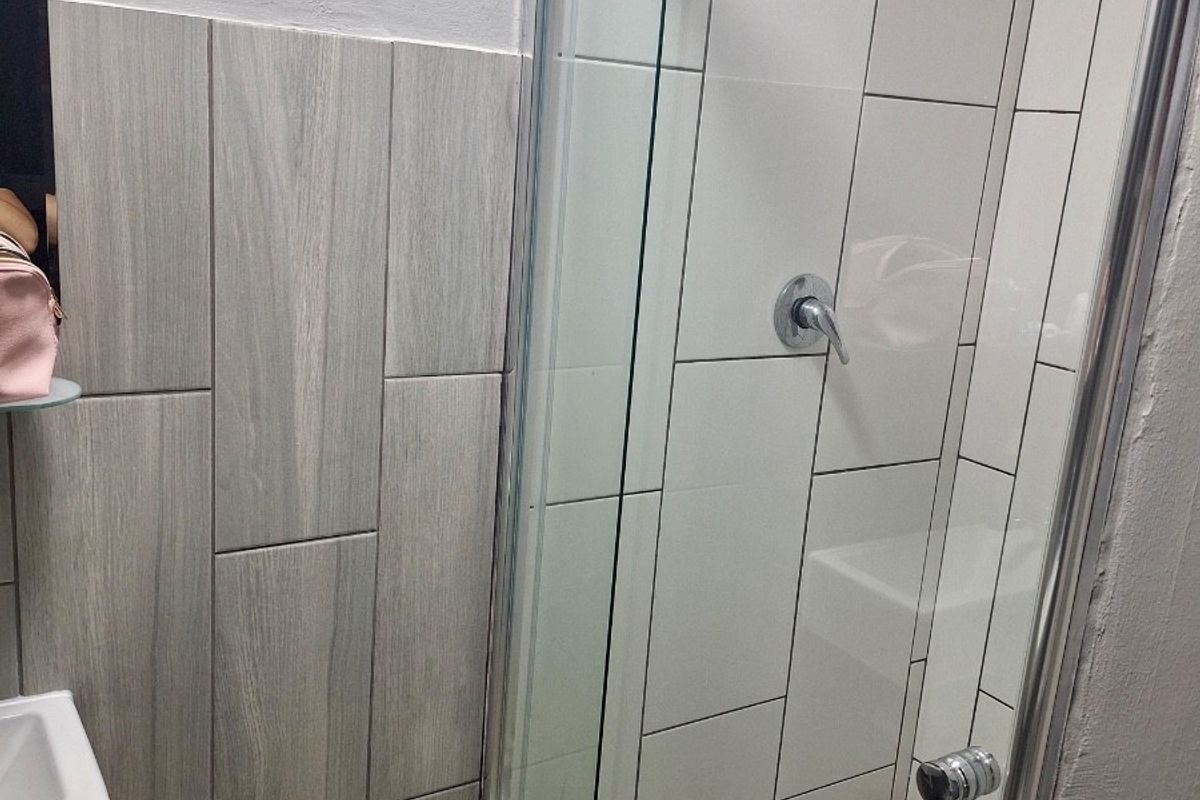 Modern bathroom featuring a glass-enclosed shower with a rain shower head, contemporary wall tiling, and a wall-mounted basin.