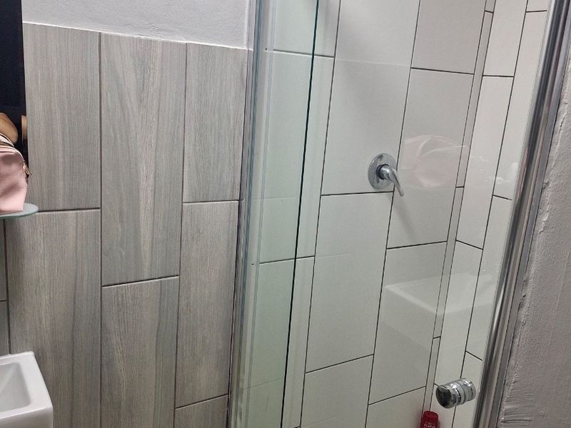 Modern bathroom featuring a glass-enclosed shower with a rain shower head, contemporary wall tiling, and a wall-mounted basin.