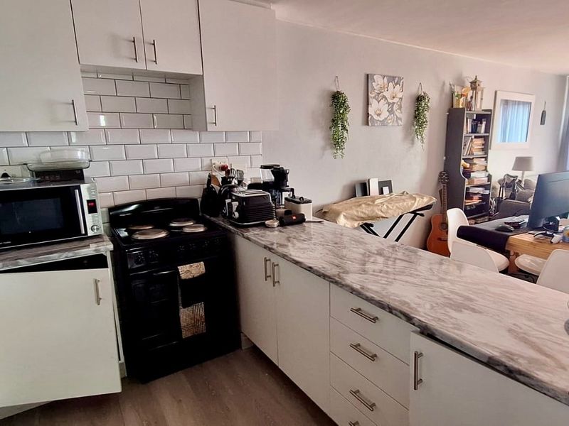 Open-plan kitchen and living area featuring white cabinetry, marble-effect countertops, subway tile backsplash, and durable laminate flooring.