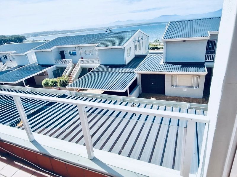 A balcony with a glass balustrade offering an elevated view over the residential complex and surrounding coastal landscape.