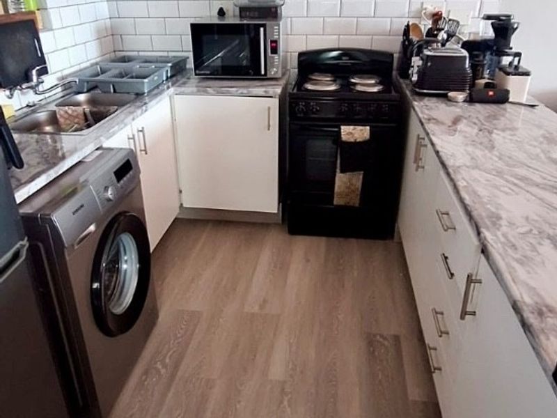 A functional kitchen featuring white cabinetry, subway tile backsplash, marble-look countertops, and modern vinyl plank flooring.