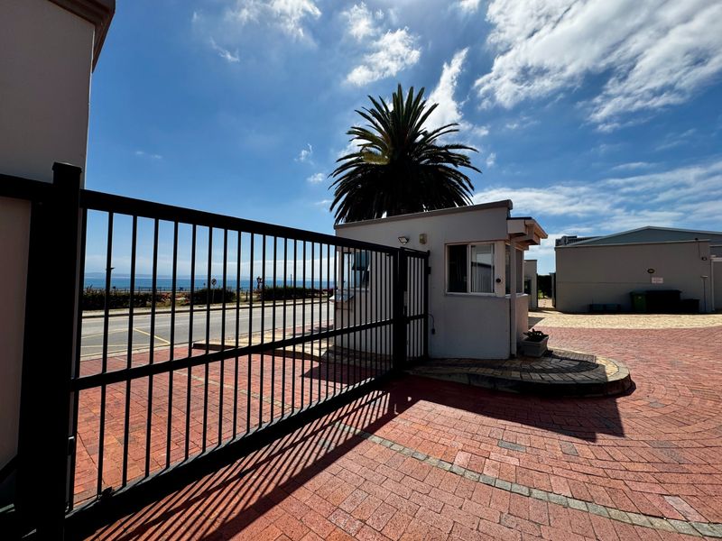 A secure gated entrance featuring a brick-paved driveway and a dedicated security guard booth, providing controlled access to the apartment complex.