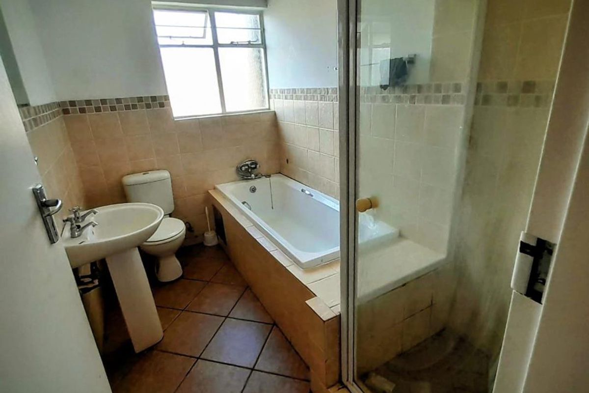 A functional bathroom featuring a built-in bathtub, separate glass-enclosed shower, pedestal basin, and toilet with tiled flooring and wall accents.