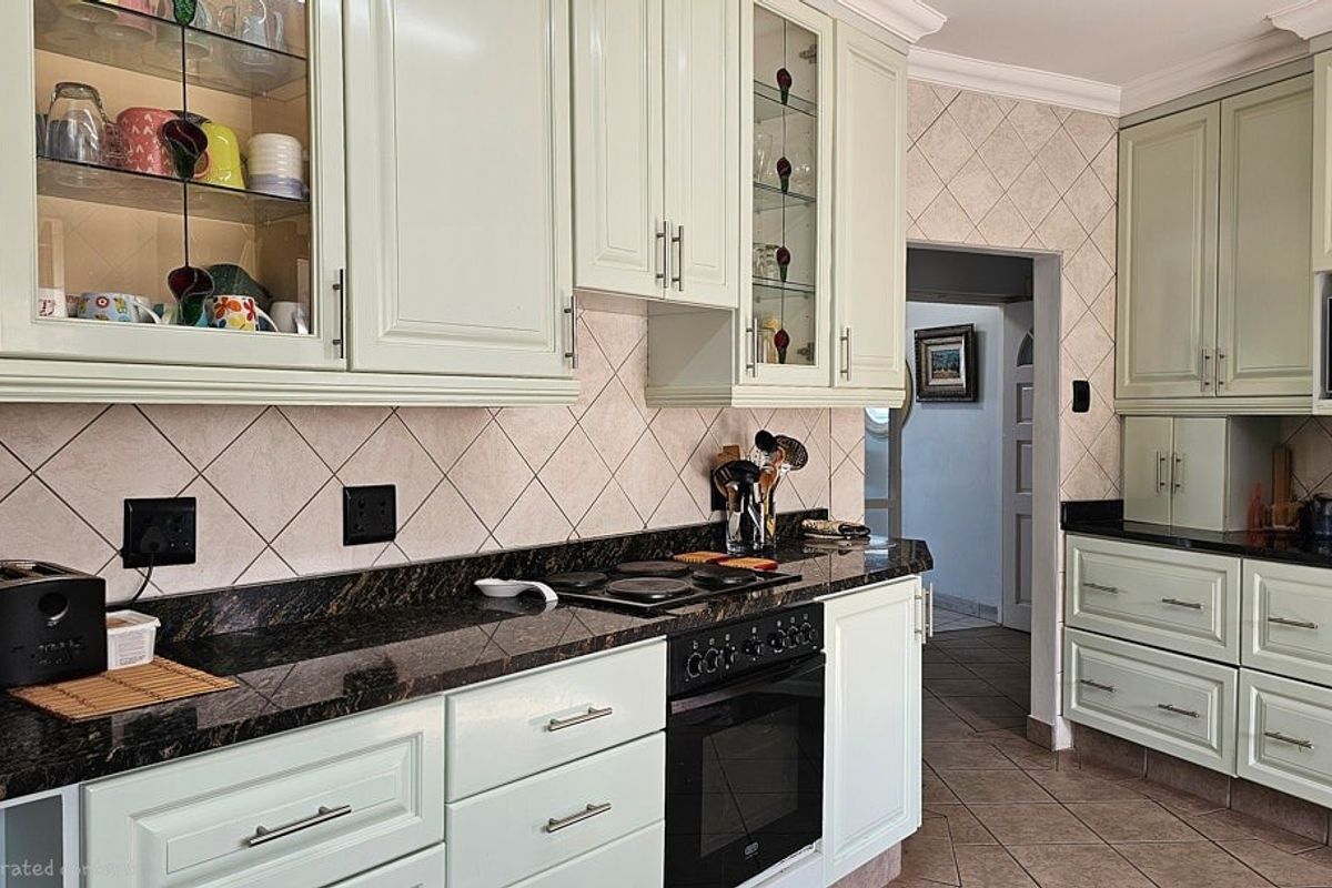 A well-maintained kitchen featuring light-toned cabinetry, dark granite countertops, a built-in oven, and a hob, complemented by tiled splashbacks and flooring.