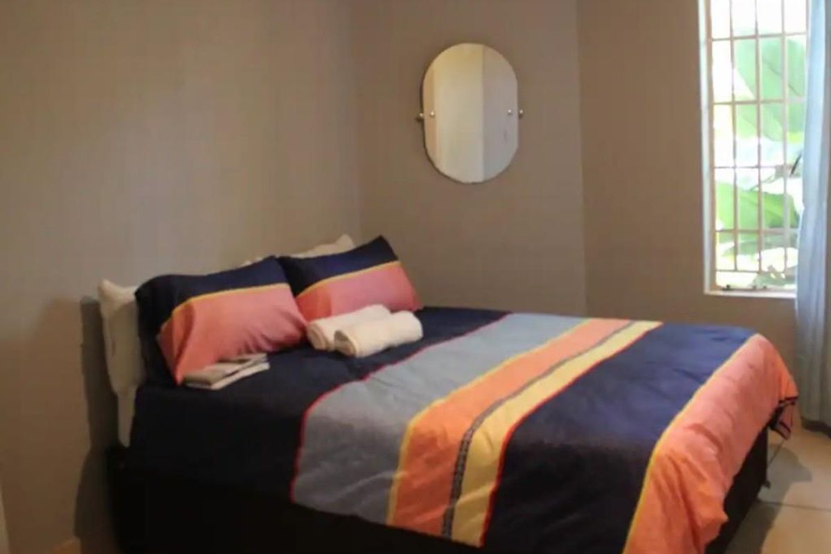 A simple bedroom featuring tiled flooring, neutral wall paint, and a window with security bars.