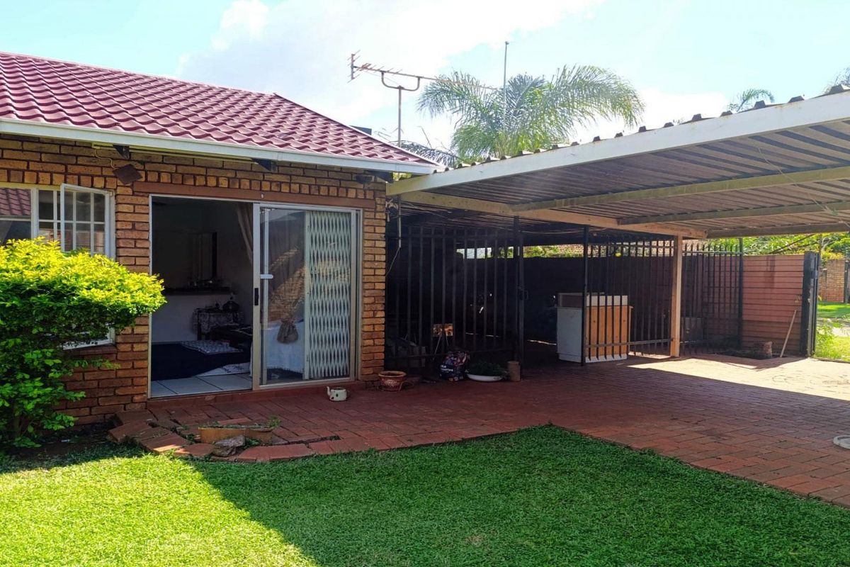 Exterior view of the property featuring a brick facade, tiled roof, paved patio area, and a covered carport structure.