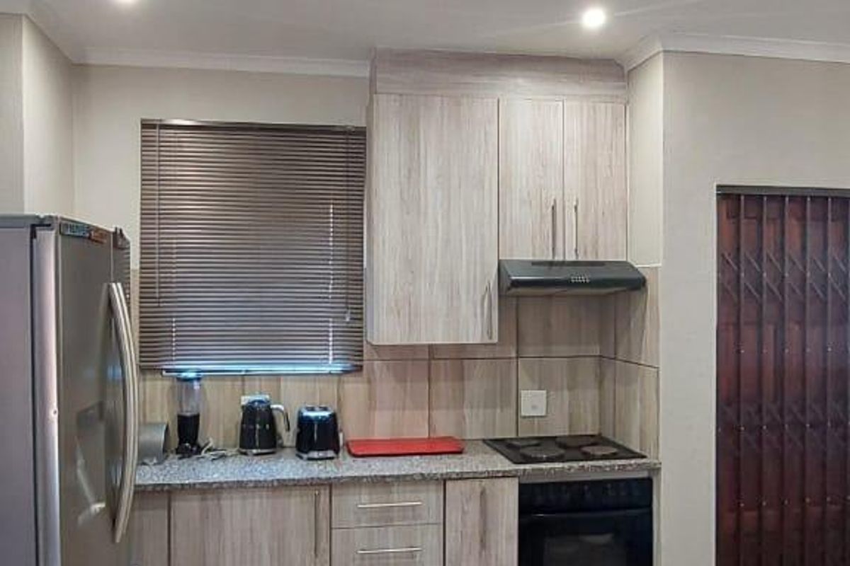 A functional kitchen featuring light wood-grain cabinetry, granite countertops, a built-in oven, and a hob with an extractor fan.