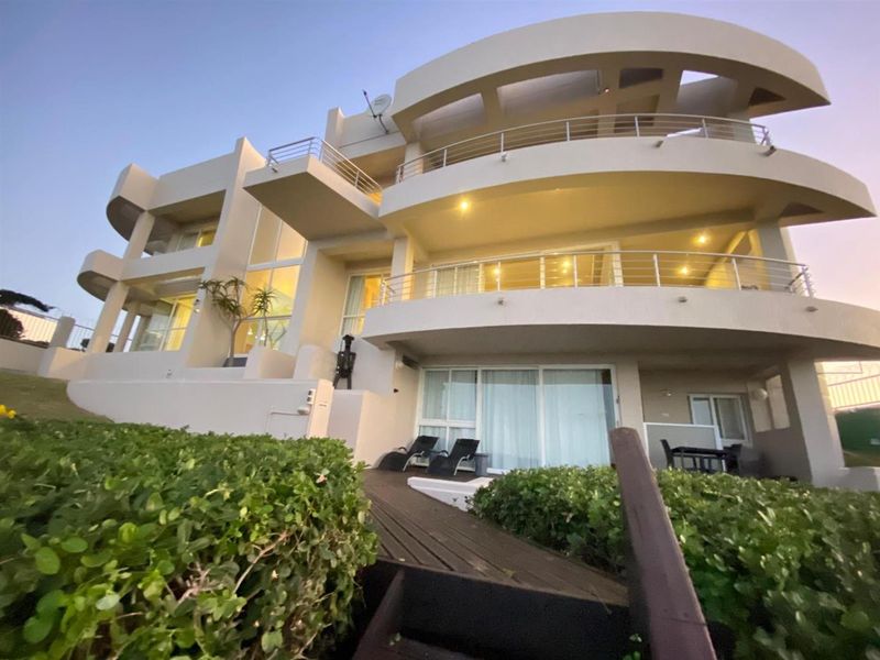 A multi-level rear exterior view of a modern house featuring curved balconies, stainless steel railings, and a landscaped garden with timber decking.