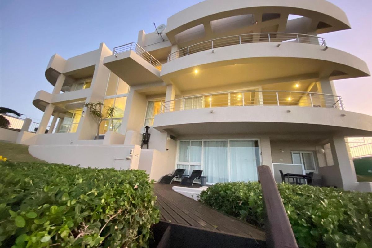 A multi-level rear exterior view of a modern house featuring curved balconies, stainless steel railings, and a landscaped garden with timber decking.