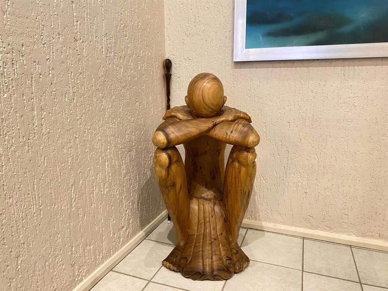 A corner of a room featuring textured wall finishes and tiled flooring, currently occupied by a decorative wooden sculpture.