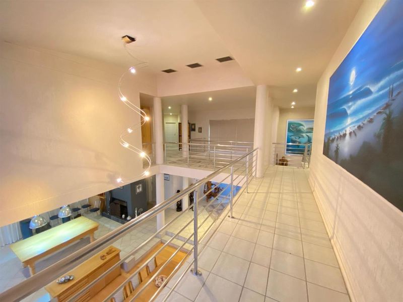 Spacious upper-level landing or hallway featuring tiled flooring, stainless steel balustrades, and an open-plan view overlooking the lower living area.