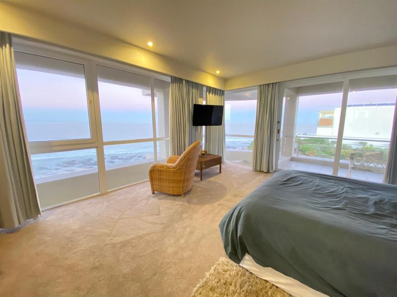 Spacious bedroom featuring expansive floor-to-ceiling windows with panoramic ocean views and direct access to a private balcony.