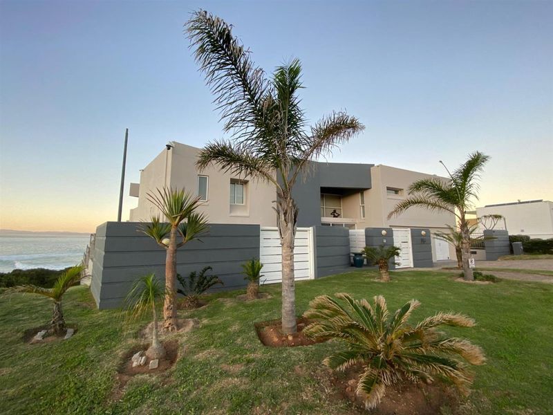 Modern coastal residence featuring a contemporary facade, landscaped front garden, boundary wall, and integrated garage, situated with ocean views.