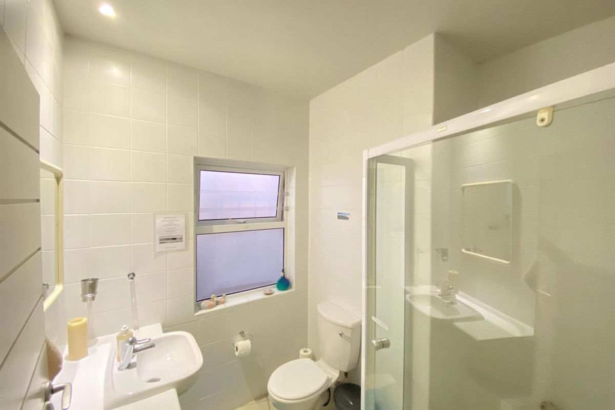 A functional bathroom featuring a shower enclosure, wall-mounted basin, and toilet with white tiled walls and recessed lighting.