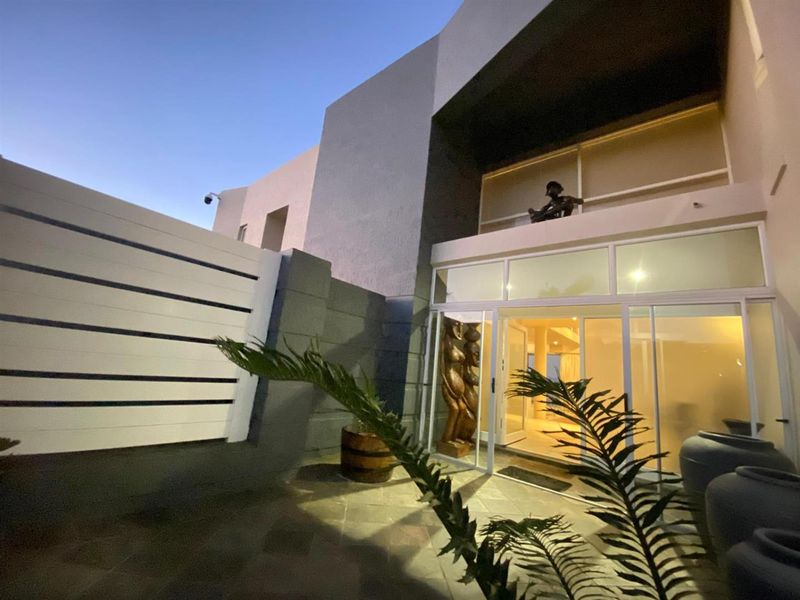 A modern rear exterior view featuring a tiled patio area, large sliding glass doors, and an upper-level balcony at dusk.