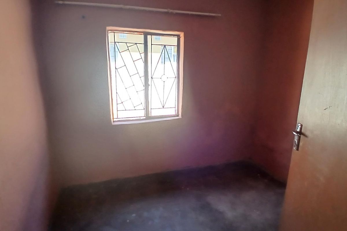 A small, empty bedroom featuring a window with security bars and a standard interior door.
