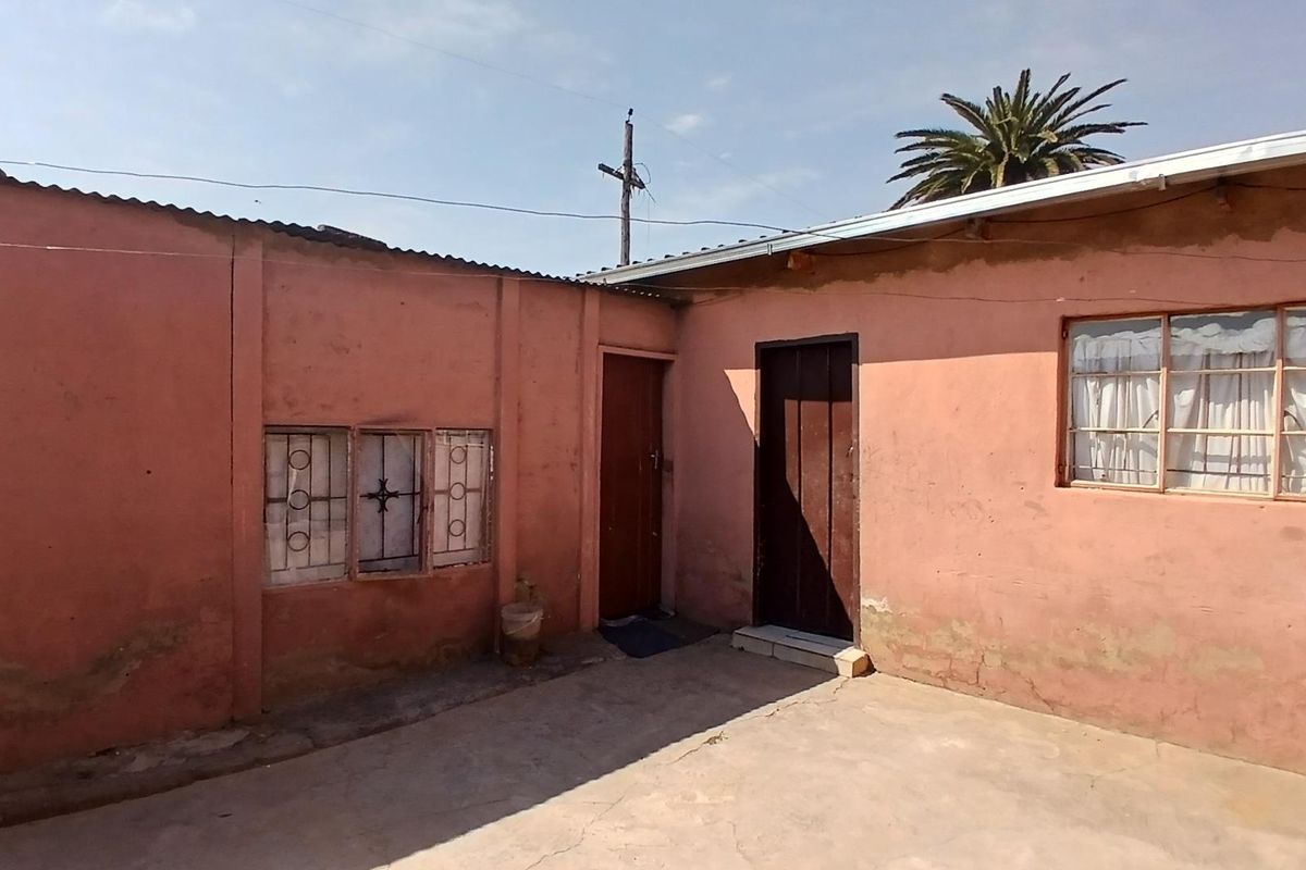 Exterior view of the rear building facade featuring concrete paving, metal security bars on windows, and two entry doors.