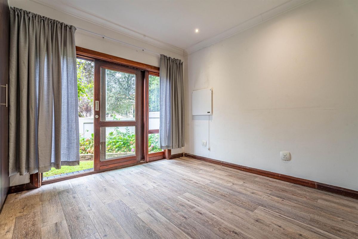 A bright, empty room featuring wood-look laminate flooring and a large timber-framed sliding door providing direct access to the garden.