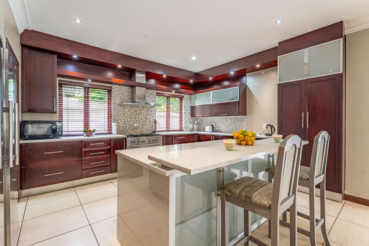 A well-appointed kitchen featuring dark wood cabinetry, stone countertops, a central island with breakfast bar seating, and a stainless steel extractor fan.