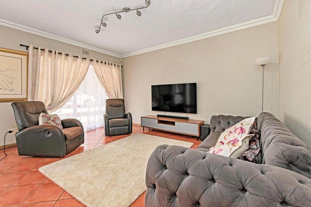 A comfortable living room featuring tiled flooring, crown molding, and a wall-mounted television setup with track lighting.