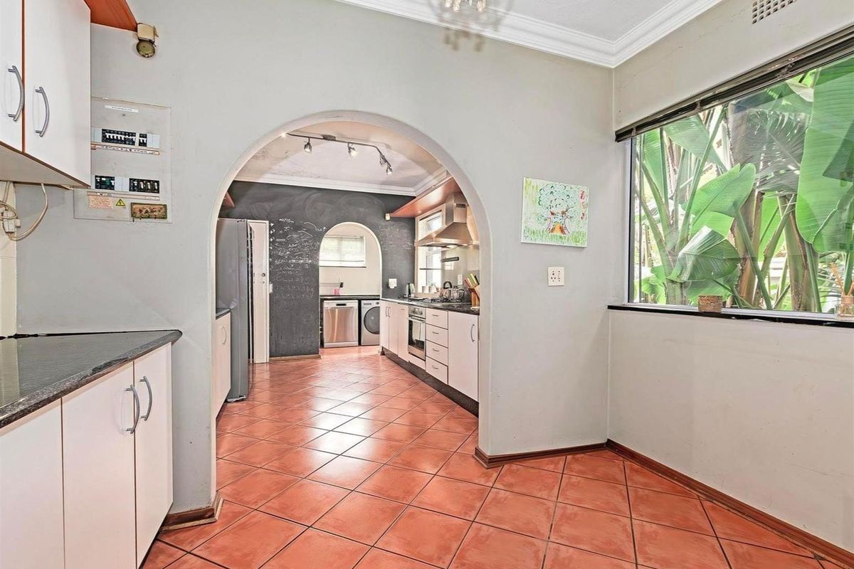 A functional kitchen featuring tiled flooring, built-in cabinetry, and an arched entryway connecting to a secondary prep or laundry area.