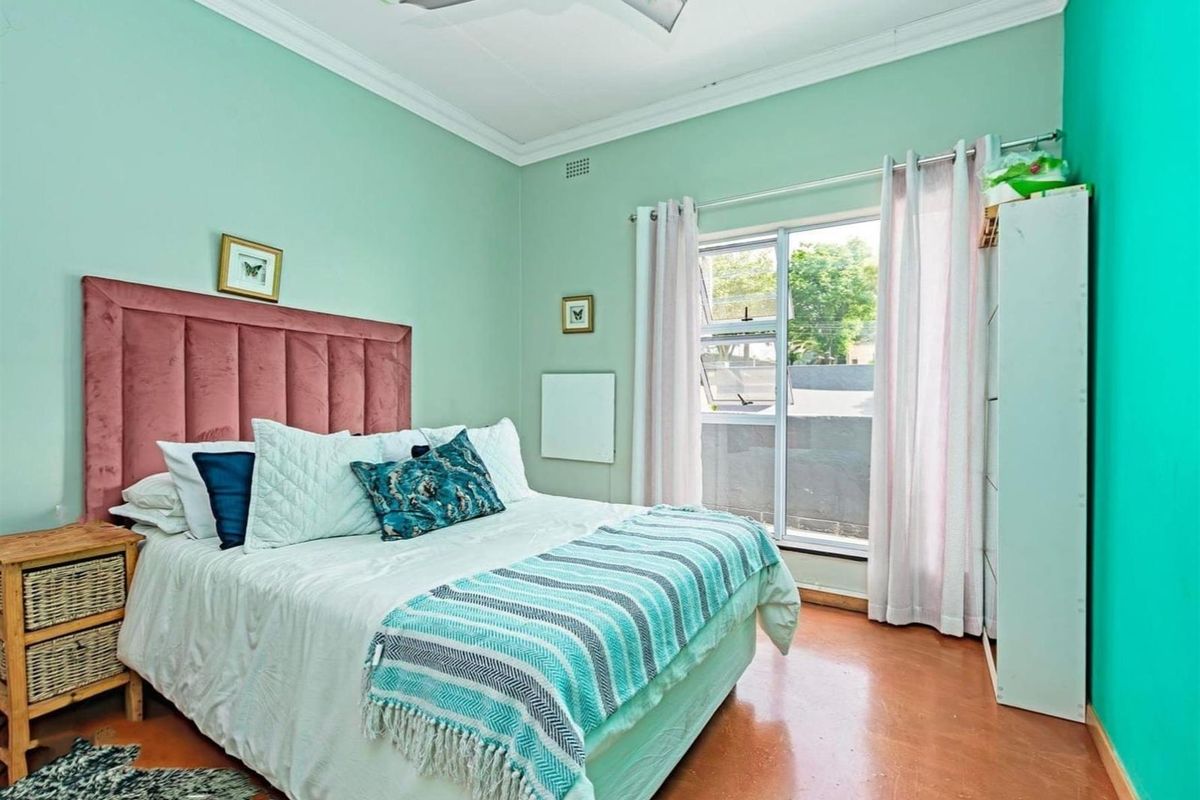 A bedroom featuring mint green walls, a ceiling fan, and a large window providing natural light.